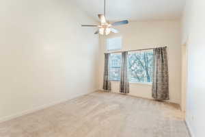 Carpeted empty room featuring high vaulted ceiling and ceiling fan