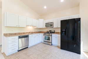 Kitchen featuring vaulted ceiling, appliances with stainless steel finishes, sink, white cabinetry, and light tile patterned flooring