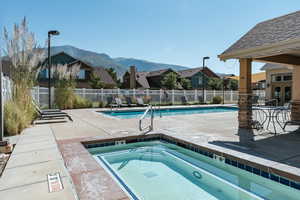 View of pool with a patio area, a mountain view, and a hot tub