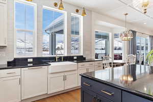 Kitchen featuring sink, hanging light fixtures, decorative backsplash, light wood-type flooring, and white cabinetry