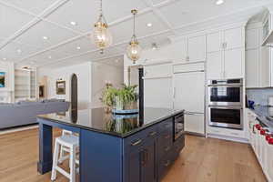 Kitchen featuring built in appliances, a center island, light wood-type flooring, and white cabinetry