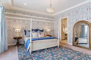 Bedroom featuring carpet, a raised ceiling, crown molding, connected bathroom, and a notable chandelier