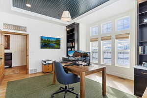 Home office featuring light hardwood / wood-style floors, crown molding, and a tray ceiling