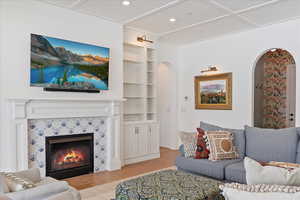 Living room featuring built in shelves, light hardwood / wood-style floors, wood ceiling, and a tiled fireplace