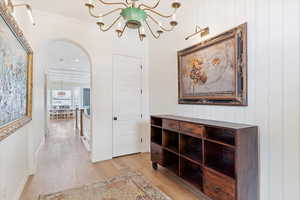 Hallway with light hardwood / wood-style floors, ornamental molding, and a chandelier