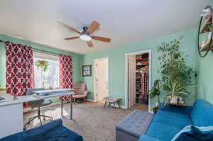 Carpeted living room with ceiling fan and a textured ceiling