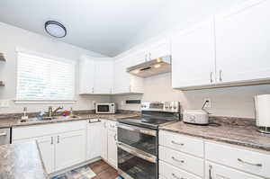 Kitchen featuring stainless steel range with electric cooktop, dark hardwood / wood-style flooring, sink, lofted ceiling, and white cabinets