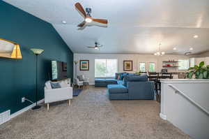 Living room with a textured ceiling, vaulted ceiling, ceiling fan with notable chandelier, and carpet floors