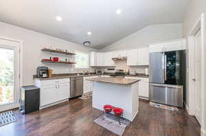 Kitchen with white cabinets, appliances with stainless steel finishes, vaulted ceiling, and dark wood-type flooring