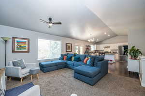 Carpeted living room featuring lofted ceiling, ceiling fan with notable chandelier, and a textured ceiling