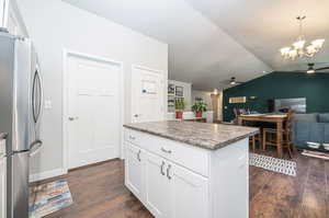 Kitchen with ceiling fan with notable chandelier, stainless steel fridge, white cabinetry, and lofted ceiling