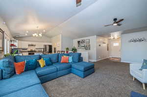 Carpeted living room featuring ceiling fan with notable chandelier, lofted ceiling, and a textured ceiling