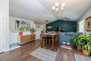 Dining area with dark wood-type flooring, ceiling fan with notable chandelier, lofted ceiling, and a textured ceiling