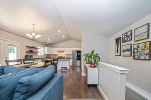 Living room with lofted ceiling, dark hardwood / wood-style floors, an inviting chandelier, and a textured ceiling