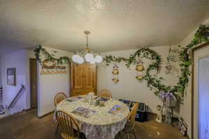 Dining space featuring dark colored carpet, a notable chandelier, and a textured ceiling