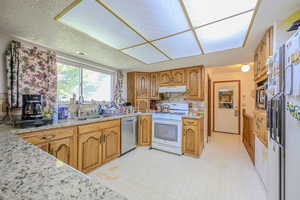 Kitchen featuring white appliances, light stone countertops, and sink