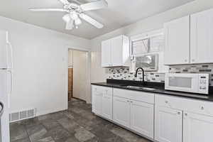 Kitchen with white appliances, backsplash, sink, white cabinetry, and ceiling fan