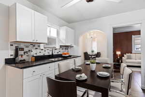 Kitchen with ceiling fan with notable chandelier, white cabinets, backsplash, sink, and light tile patterned flooring