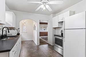 Kitchen featuring stainless steel range with electric stovetop, white fridge, ceiling fan with notable chandelier, white cabinetry, and sink