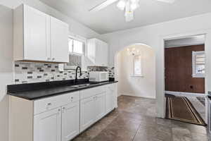 Kitchen featuring ceiling fan with notable chandelier, tasteful backsplash, sink, and white cabinets