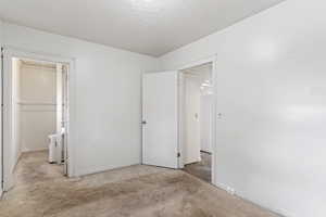 Unfurnished bedroom with a textured ceiling, a closet, a walk in closet, and light carpet