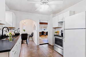 Kitchen with ceiling fan with notable chandelier, white cabinetry, sink, white fridge, and electric stove