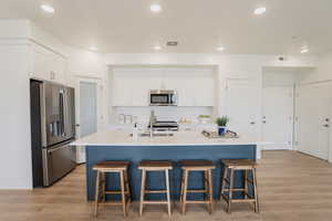 Kitchen featuring a kitchen island with sink, stainless steel appliances, white cabinets, and light hardwood / wood-style floors