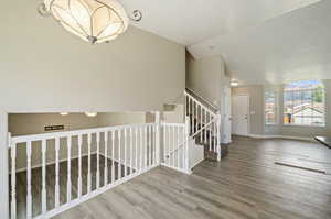 Staircase featuring lofted ceiling, wood-type flooring, and a notable chandelier