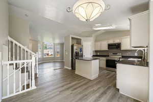 Kitchen with light hardwood / wood-style flooring, a center island, stainless steel appliances, a chandelier, and lofted ceiling