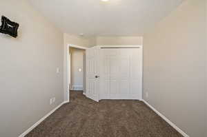 Unfurnished bedroom featuring a textured ceiling, dark colored carpet, and a closet