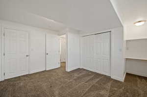 Unfurnished bedroom with a closet, dark colored carpet, and a textured ceiling