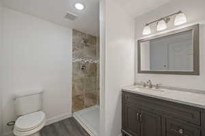 Bathroom with hardwood / wood-style floors, toilet, a tile shower, vanity, and a textured ceiling