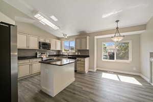 Kitchen featuring decorative light fixtures, appliances with stainless steel finishes, tasteful backsplash, a center island, and dark wood-type flooring