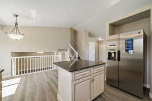 Kitchen with stainless steel refrigerator with ice dispenser, lofted ceiling, a center island, and light hardwood / wood-style floors