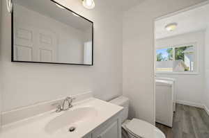 Bathroom with toilet, independent washer and dryer, vanity, a textured ceiling, and wood-type flooring