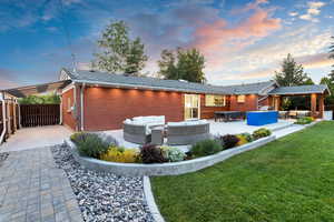 Back house at dusk featuring a patio area, a lawn, a fire pit, an outdoor kitchen and a covered area.