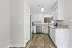 Kitchen with stainless steel appliances, white cabinets, and light stone counters