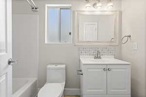 Full bathroom with  shower combination, vanity, toilet, and decorative backsplash