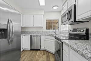 Kitchen with stainless steel appliances, white cabinets, LVP floors, and sink