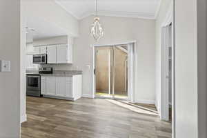 Kitchen with appliances with stainless steel finishes, white cabinets, an inviting chandelier, LVP floors, and decorative light fixtures