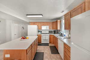 Kitchen with white appliances, a textured ceiling, light tile patterned floors, a kitchen island, and sink