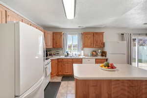 Kitchen featuring a textured ceiling, a kitchen island, white appliances, sink, and light tile patterned flooring