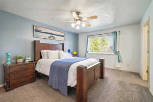 Carpeted bedroom with ceiling fan and a textured ceiling