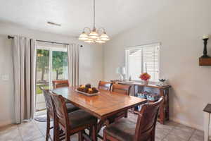 Dining area featuring lofted ceiling, a notable chandelier, light tile patterned floors, and a textured ceiling