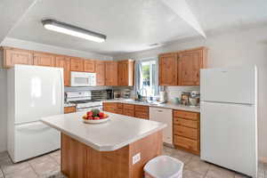 Kitchen featuring a textured ceiling, a center island, sink, and white appliances