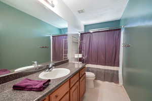 Bathroom with a textured ceiling, vanity, toilet, and curtained shower