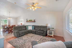 Living room with ceiling fan with notable chandelier, vaulted ceiling, a textured ceiling, and light hardwood / wood-style floors