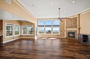 Unfurnished living room with crown molding, dark wood-type flooring, ceiling fan, and a stone fireplace