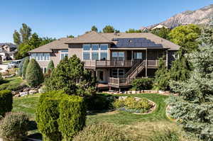 Back of house featuring a deck with mountain view, a lawn, and solar panels