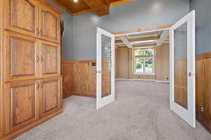 Home office featuring wooden walls, french doors, light colored carpet, beamed ceiling, and coffered ceiling